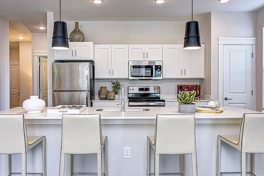JC Hart's experienced staff is here to help you find and move into wonderful units like this one at Wheelhouse Apartments on the Monon in Westfield. White kitchen with overhead lighting and seating in a new apartment